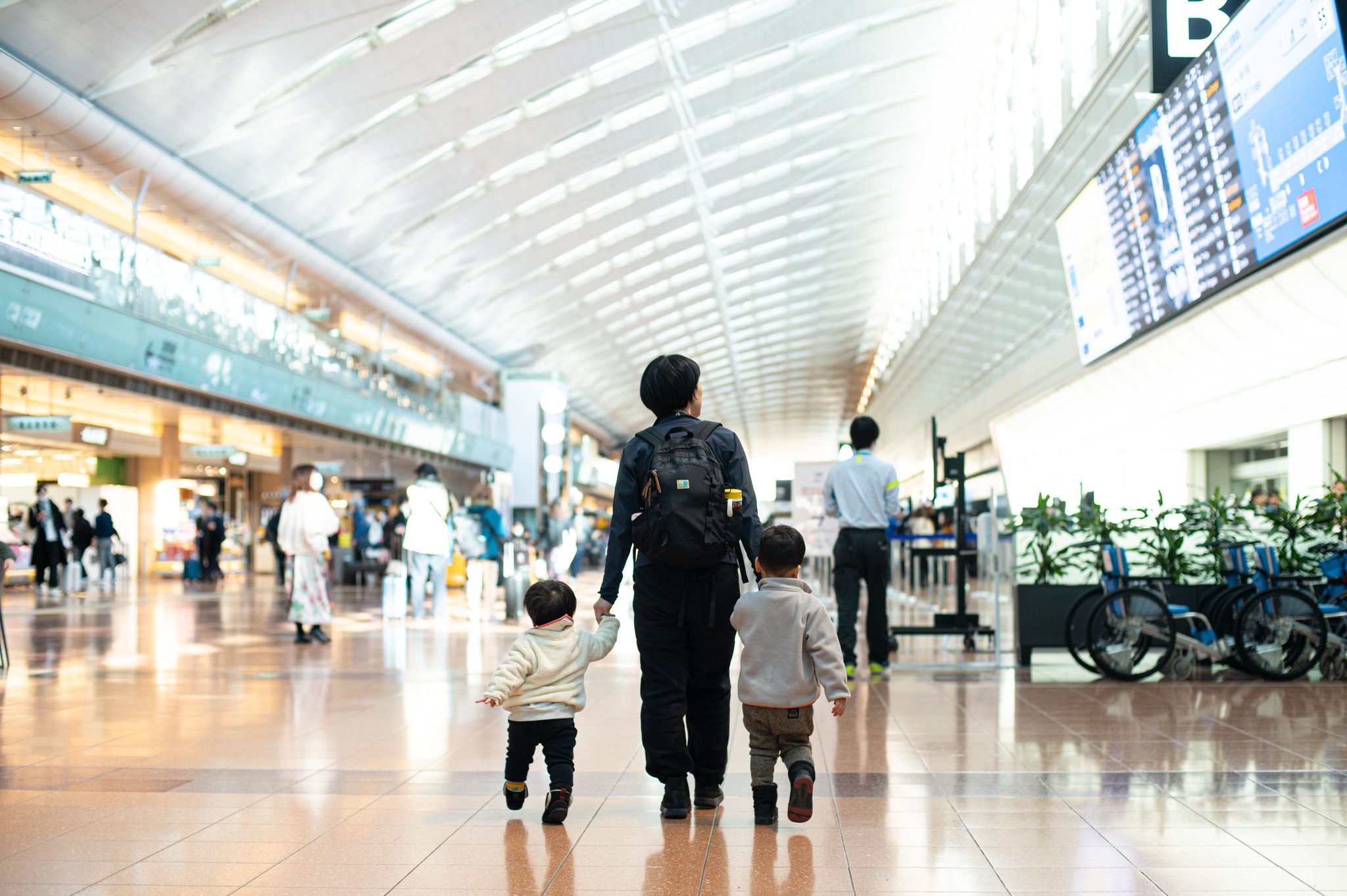 空港の出発ロビーを、父と手をつないで歩くふたりの男の子