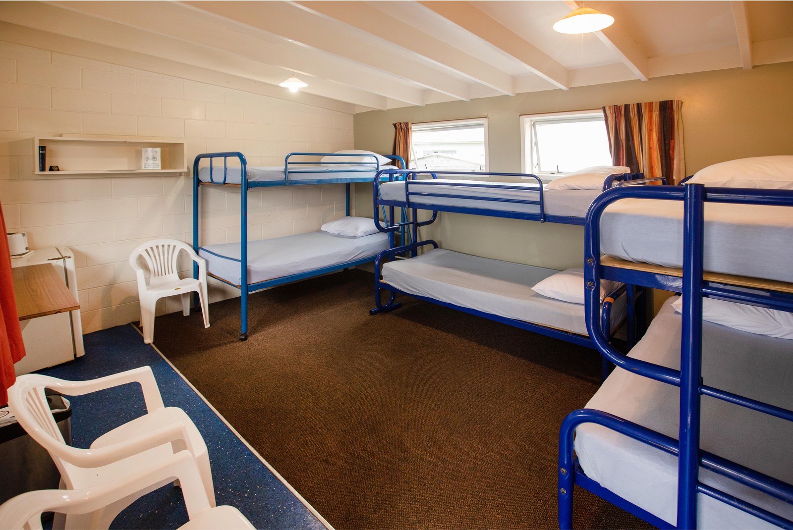 Tāhuna Beach Holiday ParkのBasic Cabin Sleeps 6。青い2段ベッド3台とテーブルがある室内