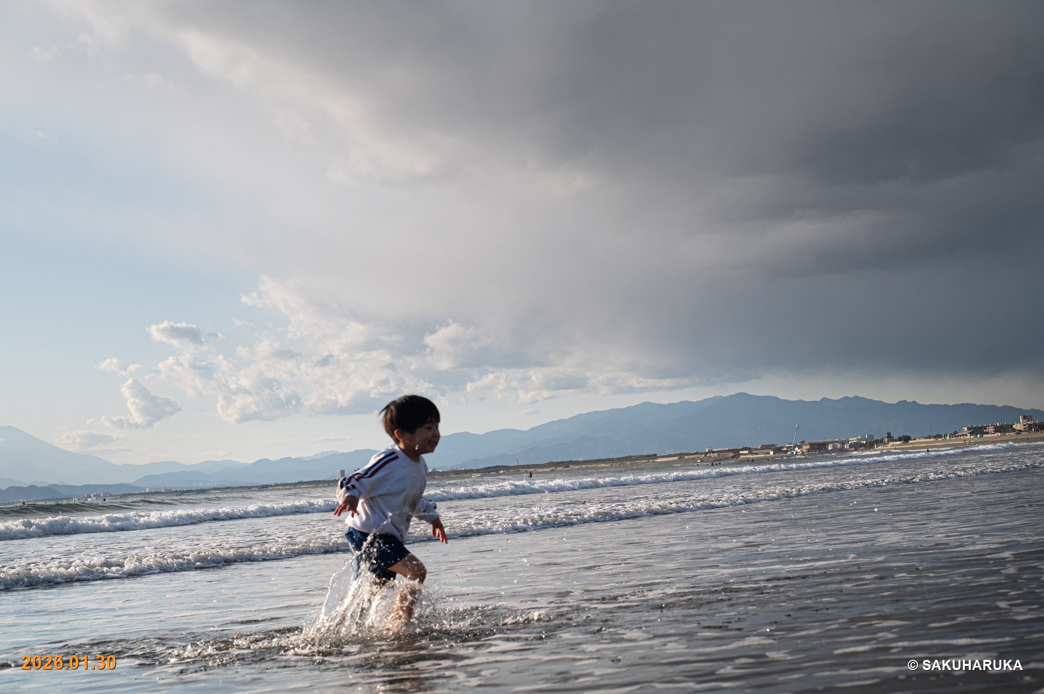 曇り空の海で水しぶきをあげて駆ける男の子