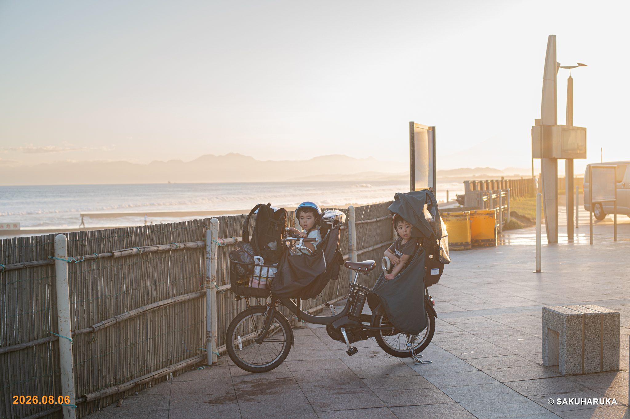 夕暮れの海辺の道、自転車の前と後ろの席に乗った兄弟